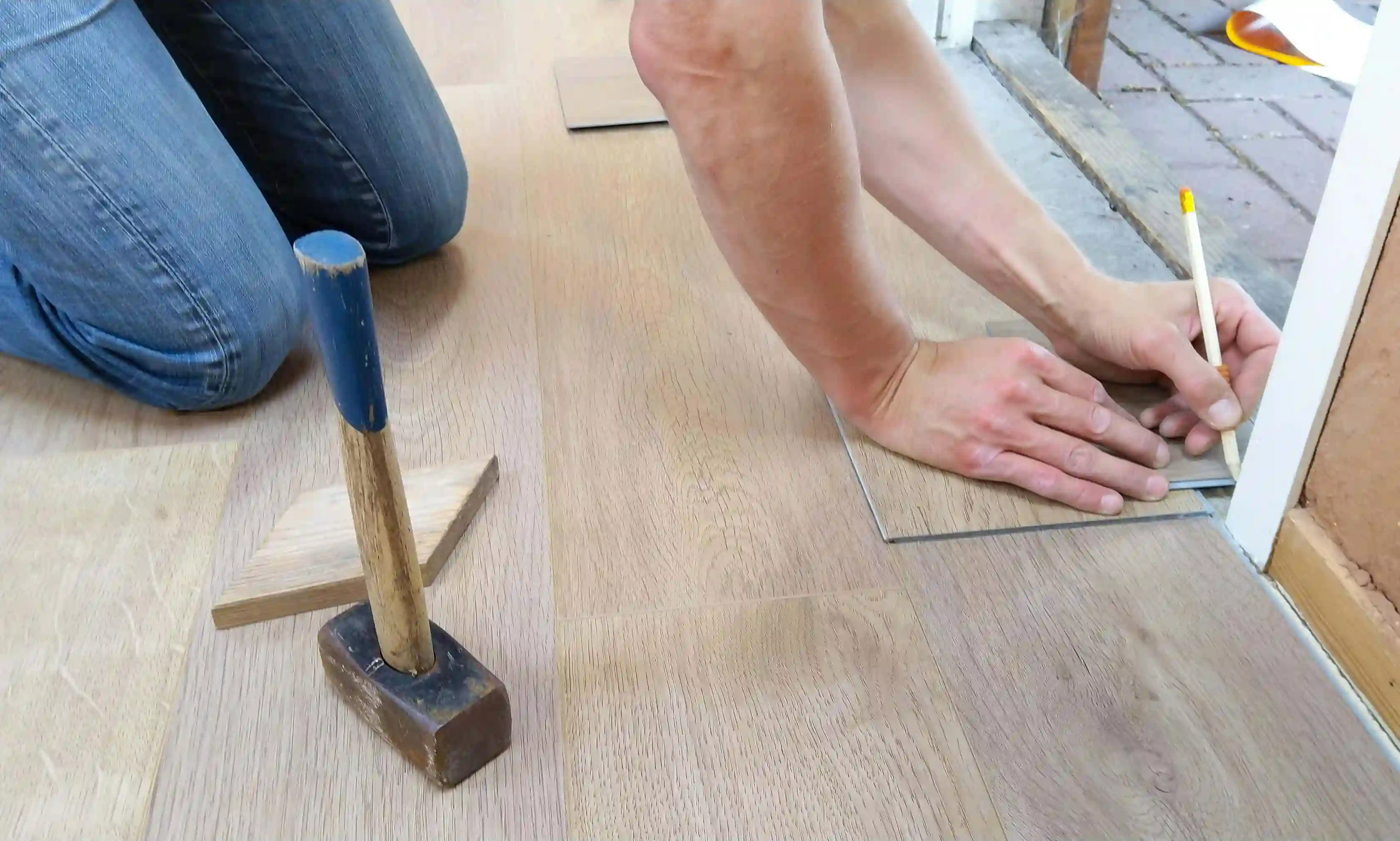 Two people installing a light-colored wood floor in a home.
